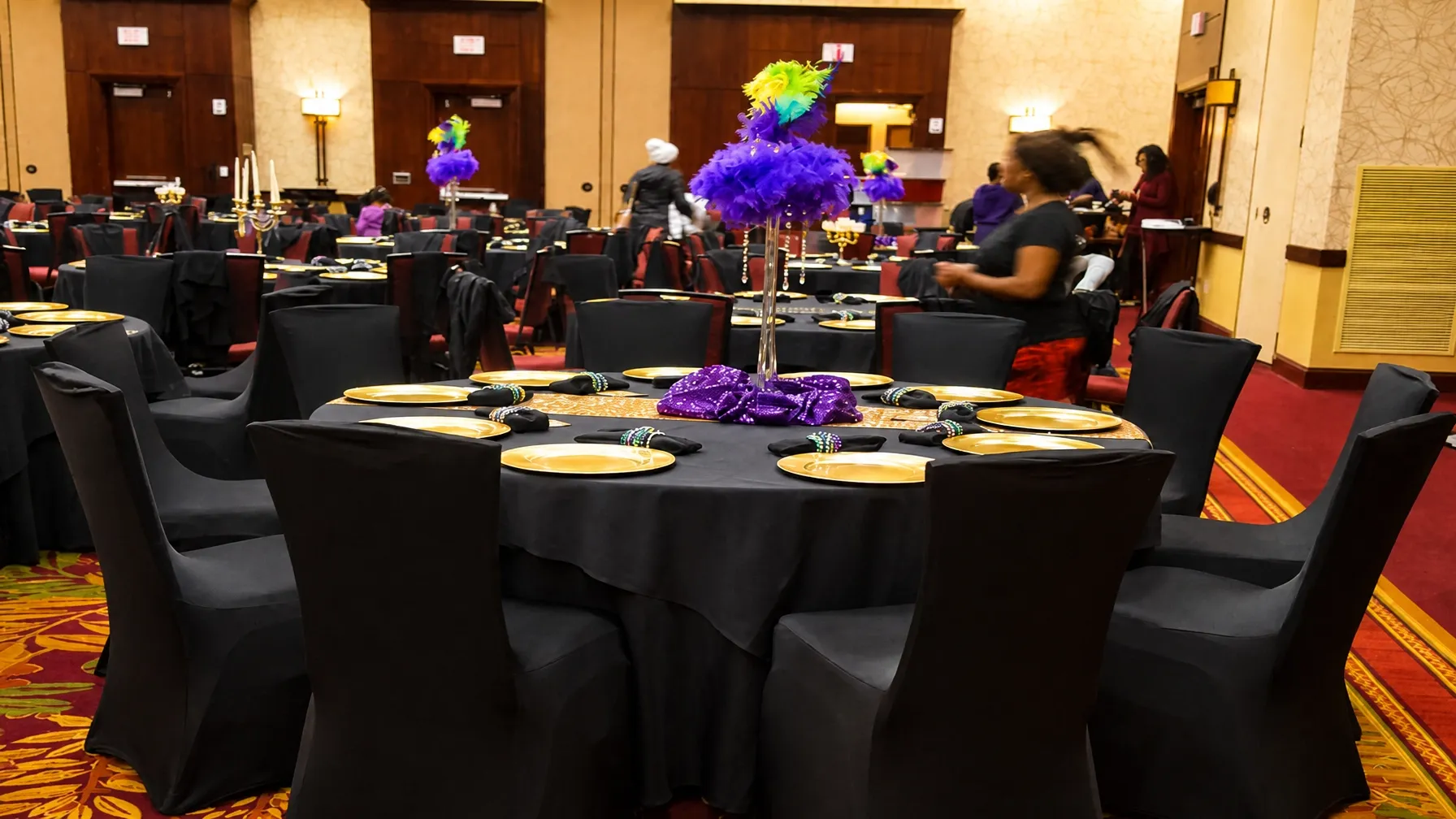 Full event room and stage styling with round tables, black linens, and colorful floral accents